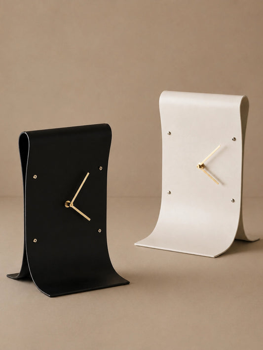 Black and white curved table clocks with gold-tone hands against a neutral beige background.
