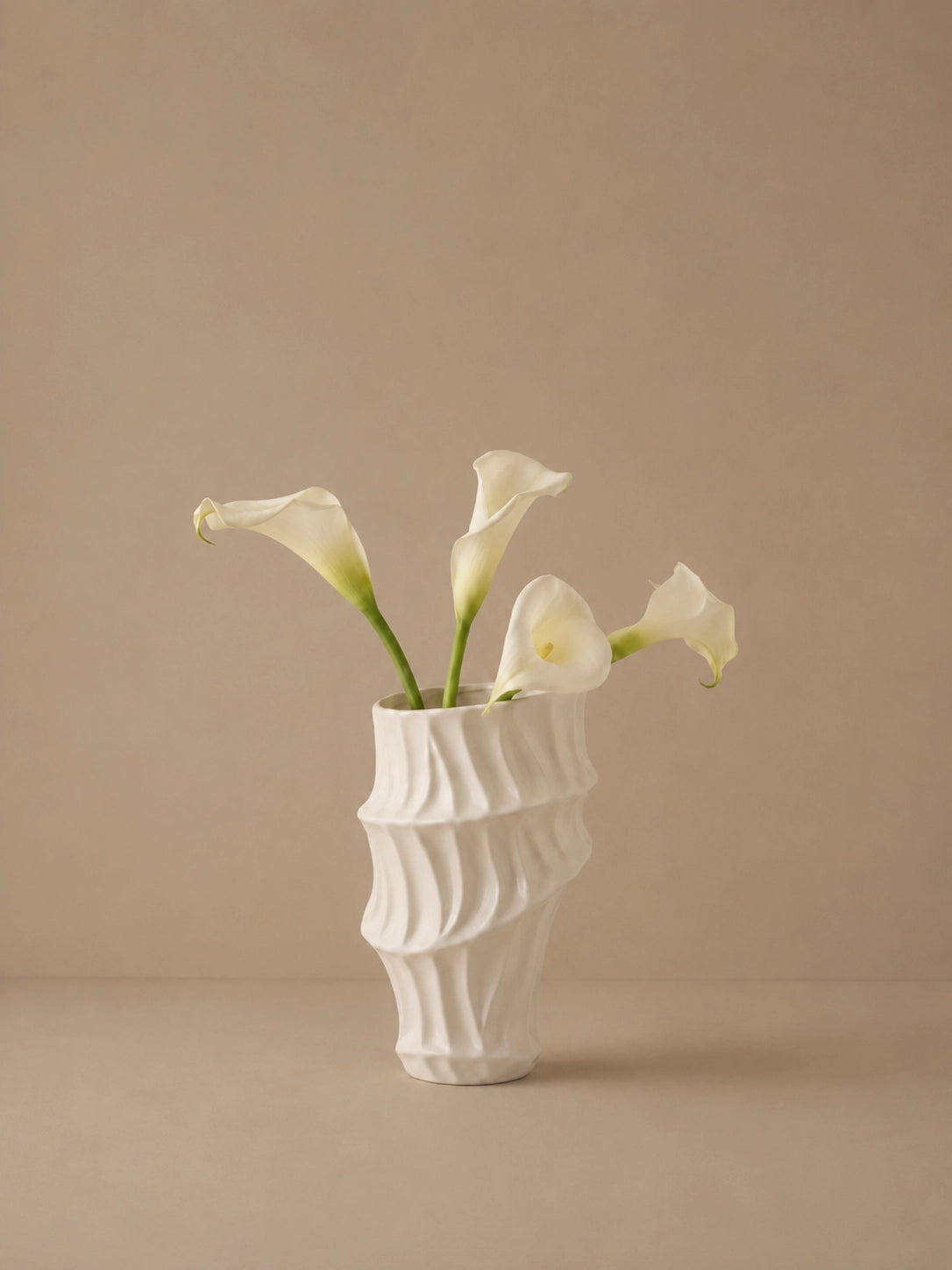 Off-white sculptural ripple vase holding white flowers against a warm beige background.