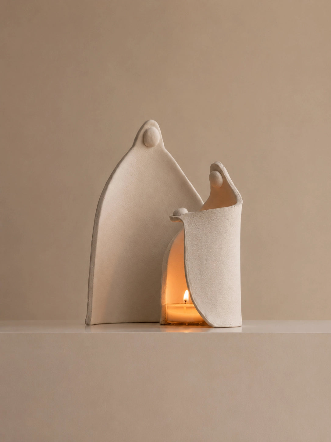 Abstract ivory sculptural candle holder with two curved figures illuminated by a warm tealight