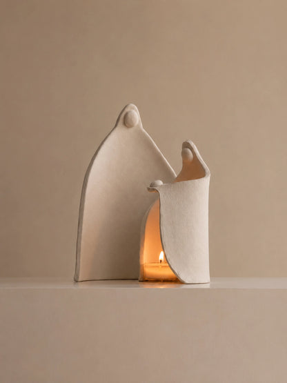 Abstract ivory sculptural candle holder with two curved figures illuminated by a warm tealight